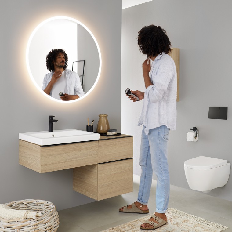 男人看向圆形发光的 Geberit Option 镜子 男人看向圆形发光的 Geberit Option 镜子