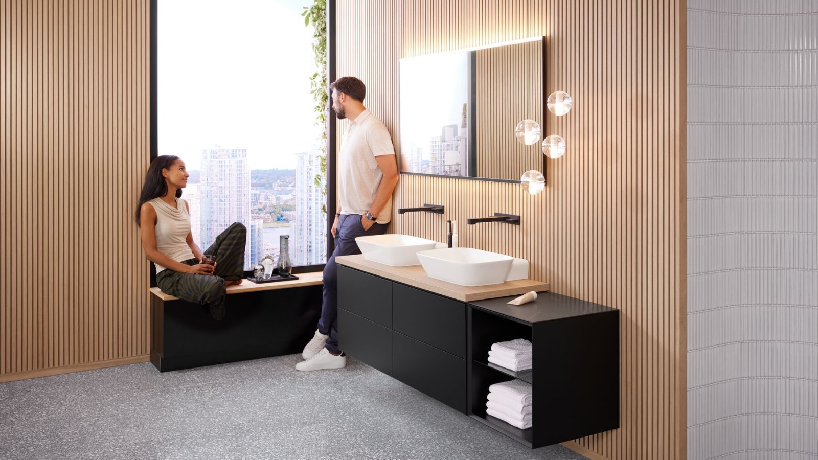 Woman sitting on windowsill in bathroom with Geberit ONE products, talking to man Woman sitting on windowsill in bathroom with Geberit ONE products, talking to man